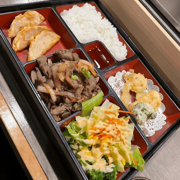 A Kumagoro bento box with gyoza, rice, beef, tempura, and a fresh salad.