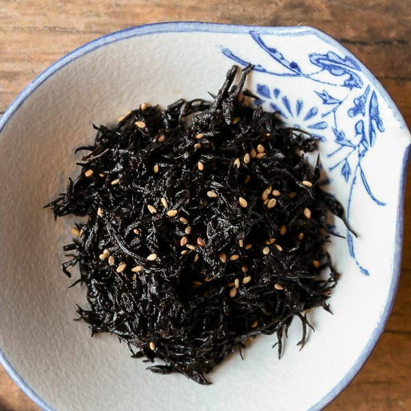 A white and blue patterned bowl filled with dark hijiki seaweed and sesame seeds.