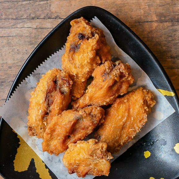 Crispy Kumagoro fried chicken wings, golden brown and glistening, served on a black plate with parchment paper.