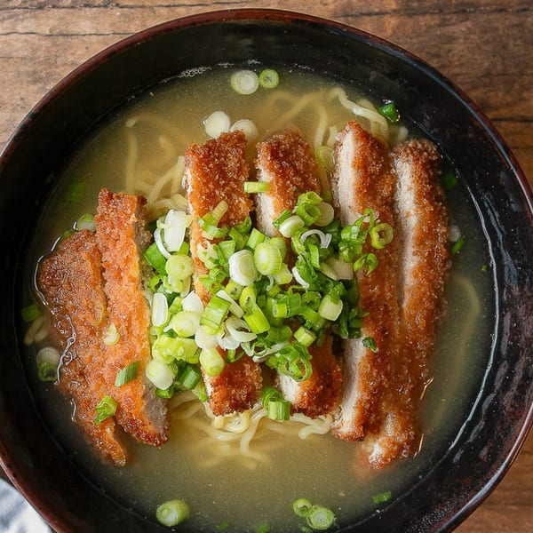 Kumagoro ramen with crispy tonkatsu slices and fresh green onions in a dark bowl.