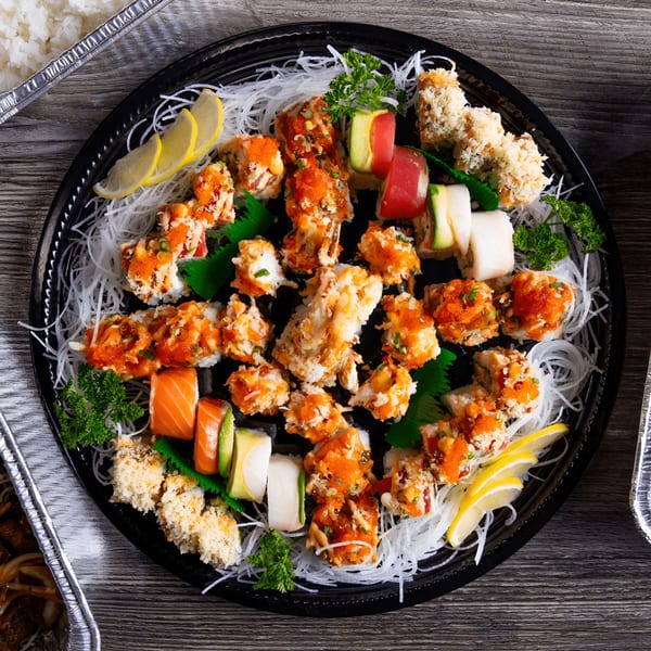Kumagoro sushi platter with various rolls, including spicy tuna, salmon, and tempura, garnished with lemon and parsley.