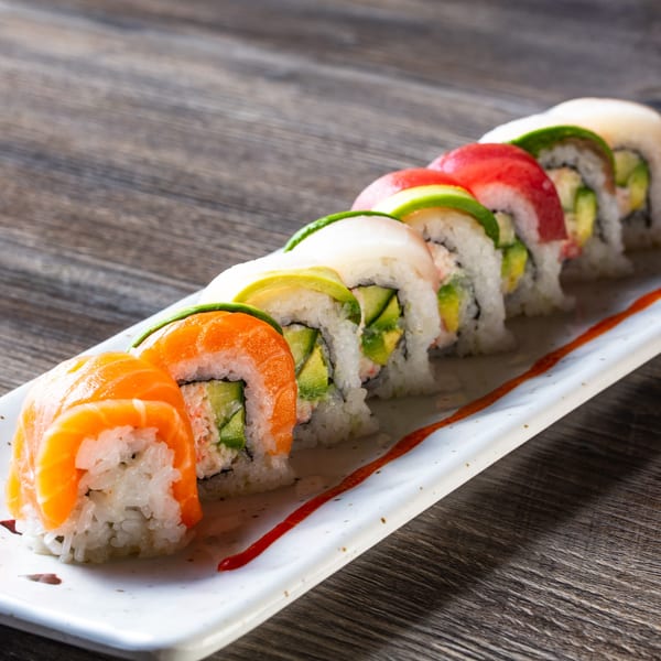 A row of colorful Kumagoro sushi rolls with salmon, tuna, and avocado on a white plate.