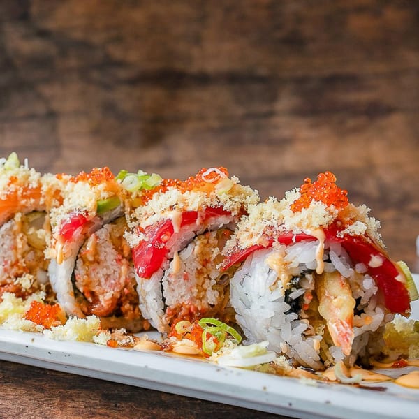 Kumagoro sushi roll with shrimp tempura, tuna, avocado, roe, and crunchy topping on a white plate.
