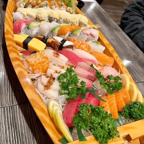 A large Kumagoro sushi boat filled with various sushi rolls, sashimi, and nigiri, garnished with lemon and parsley.