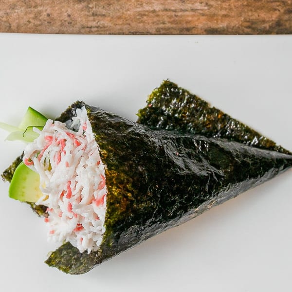 Kumagoro's hand roll sushi, filled with crab meat, avocado, and cucumber, on a white surface.