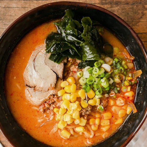 Overhead view of a Kumagoro ramen bowl with pork, corn, seaweed, and green onions.