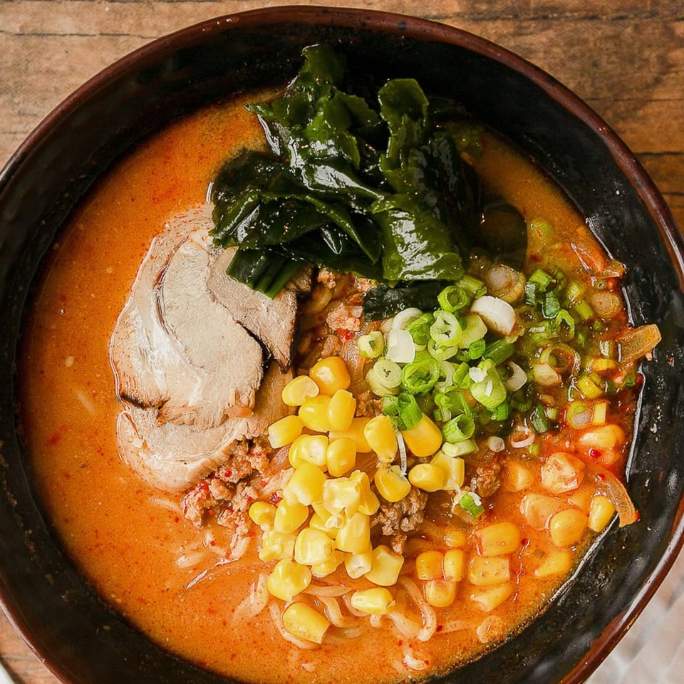 Overhead view of a Kumagoro ramen bowl with pork, corn, seaweed, and green onions.