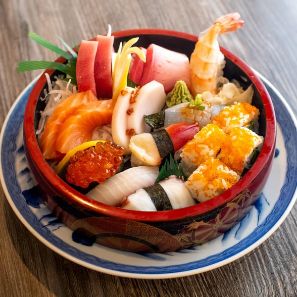A vibrant Kumagoro sushi and sashimi bowl, featuring tuna, salmon, shrimp, and various rolls.